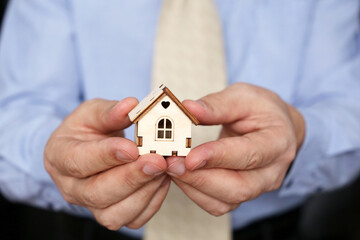 Real estate agent, wooden house in male hands. Man in office clothes with house model, purchase or rental home