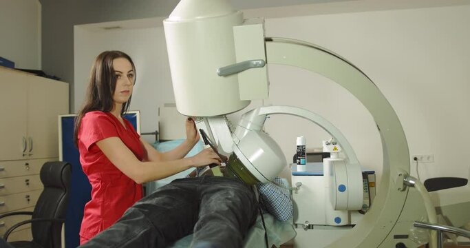 Female doctor uses modern lithotriptor to break up kidney or gallbladder stones for male patient. Ultrasound lithotripsy, non-surgical treatment to crush kidney, urethra, and bladder stones.
