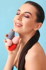 Beautiful young woman with makeup sponges on color background