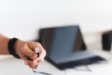 Man hand holding internet cable wire with laptop in background.