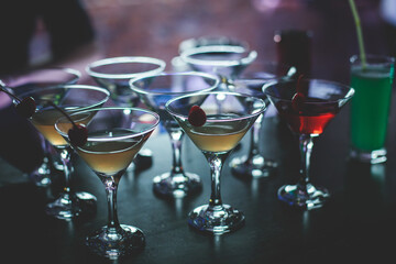 View of different coloured alcohol beverage cocktail drinks setting on bar counter in the night club party, tequila, glasses with martini, vodka, spritz and others on decorated catering banquet table