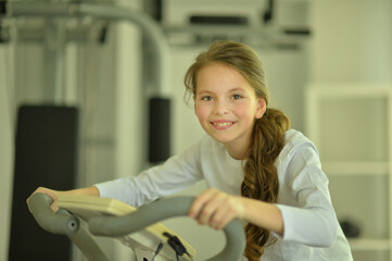 Little girl doing exercises on  bike in gym
