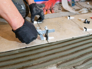 Workers are using plastic clamps and wedges to leveling the ceramic tile on the floor. Tile leveling system.