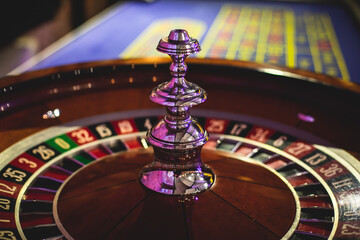 A close-up vibrant image of multicolored casino table with roulette in motion, with casino chips. the hand of croupier, money and a group of gambling rich wealthy people playing in the background