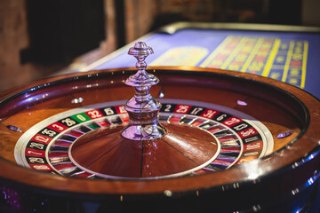 A close-up vibrant image of multicolored casino table with roulette in motion, with casino chips. the hand of croupier, money and a group of gambling rich wealthy people playing in the background