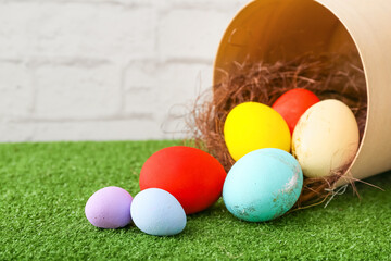 Box with beautiful Easter eggs on grass against light background