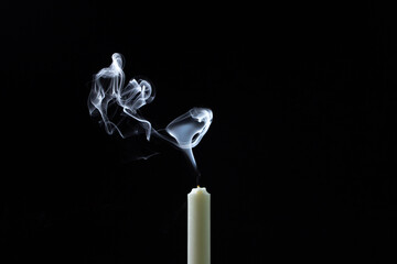 Smoke from a candle on a black background. An extinguished candle on a dark background. White smoke