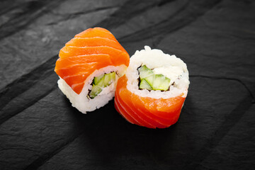 Salmon sushi maki rolls with avocado and cucumber filling on black background