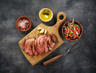 Sliced BBQ steak medium rare with salad and garlic on the grey background. Hip steak on wooden...