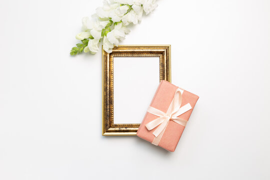 Anniversary concept. Empty photo frame with gift, snapdragon flowers on white background. flat lay, top view, copy space