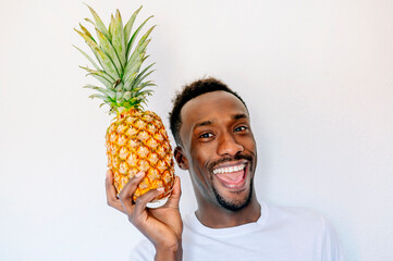 Cheerful man smiling looking at camera and holding a natural pineapple next to his face