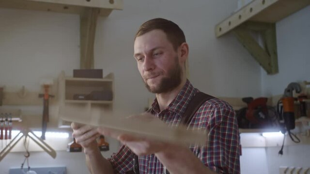 Bearded man in plaid shirt works with wooden blocks in carpenter shop. Checks the equality of the material