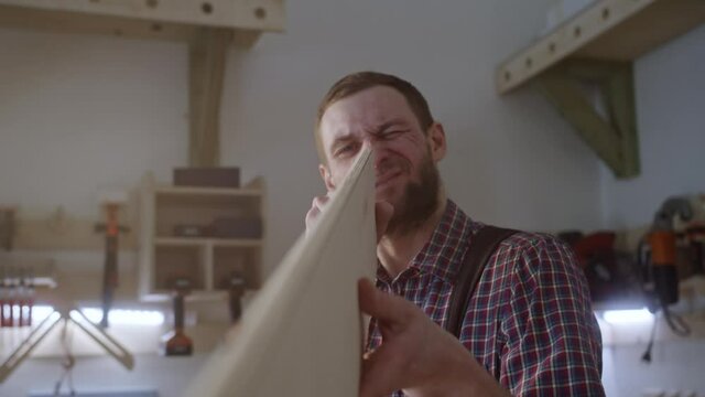 Bearded man in plaid shirt works with wooden blocks in carpenter shop. Checks the equality of the material