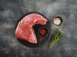 Raw beef tri-tip steak for BBQ on wooden board with salt, garlic and pepper, top view.