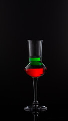 Green and red cocktail in the glass for grappa with reflection on black background.Close up of colored alcohol shot with copy space.