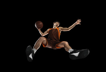 Obraz premium Young professional basketball player in action, motion isolated on black background, look from the bottom. Concept of sport, movement, energy and dynamic.