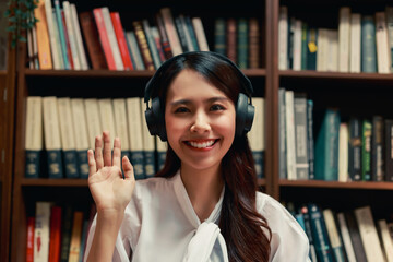 attractive asian woman using laptop computer and headphone making video conference in the reading room.