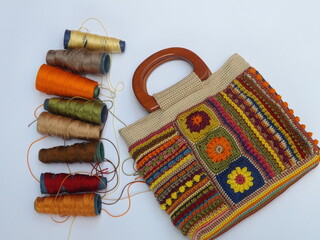 Image of colorful crochet bag made of leftover yarns against white surface. Concept of creativity, something bright colorful, and utilization leftover things. Yarns also appeared in frame.