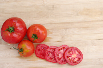 three juicy red wet tomatoes with slices on a light wood background with copy space