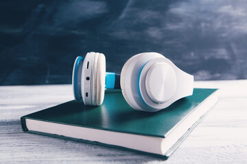 Books and modern headphones on light blue background, top view.