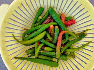 Many number of green chilli peppers on yellow bowl