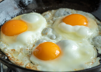 Keto meal eggs frying on hot cast iron frying pan, three fried yellow yolk, ketogenic diet, fat protein breakfast. Macro side view of cooking in the kitchen home interior, authentic lifestyle