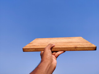 South Indian young man giving wooden chopping board .Cloud background
