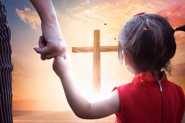 Child's hand holding mother's finger on blurred The cross of jesus christ background.