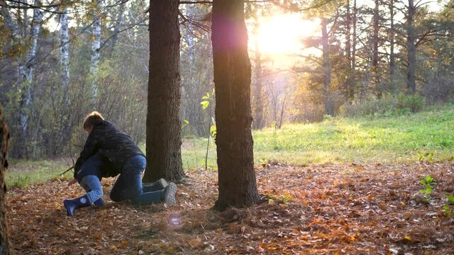 A teenager plays with a child, runs in the Park around a tree and catches up with him. The sun's rays penetrate the pine forest. Laughter and joy of the whole family.