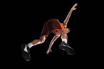 Young professional basketball player in action, motion isolated on black background, look from the...