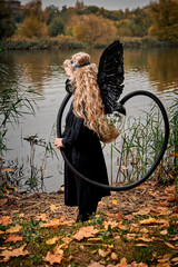 little girl with white rose with angel wings in respirator mask near the lake in autumn.