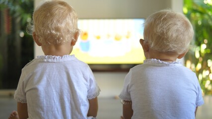 Back view of two blonde toddlers watching something on a big flat screen. Leisure activities 