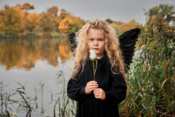 little girl with white rose with angel wings near lake in autumn