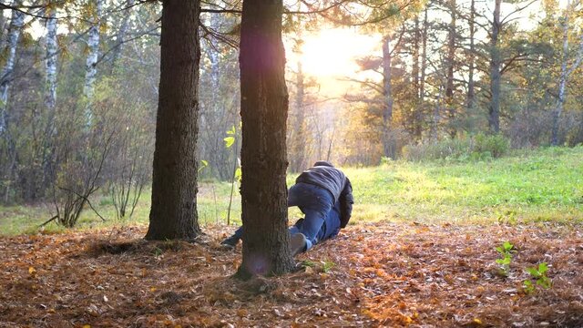 A teenager plays with a child, runs in the Park around a tree and catches up with him. The sun's rays penetrate the pine forest. Laughter and joy of the whole family.