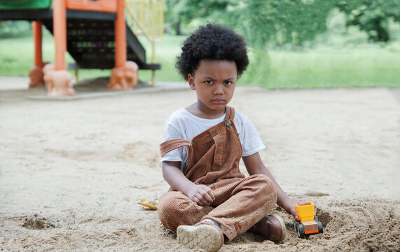 African Little Boy Stare At The Camera With An Angry Expression While Playing Sand With Toys Loader On Playground Outdoors In The Park On A Sunny Day