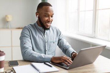 Black Businessman Working On Laptop Wearing Earbuds Sitting In Office