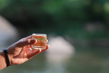 Close up of man hand holding small bubble beer glass against a natural background. Drinking beer in...