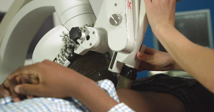 Close up cropped image of lying African man patient having procedure of lithotripsy. Hands of female doctor working with modern ultrasonic lithotripter to crush kidney or ureter stones