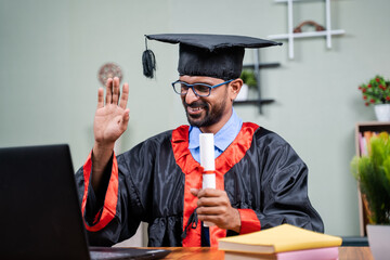 Student attending virtual graduation from laptop by holding certificate in graduation dress from...