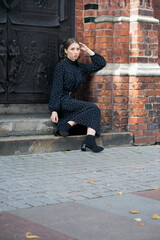 A girl in a black dress sits on the steps of an old building