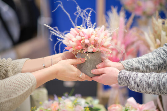 business owner selling behind counter with her bouquet of dried flowers at local market of craftsmen, small business. young woman entrepreneur sells floral holiday composition.