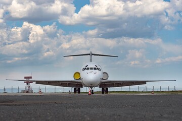 Front view of white airplane. Jet commercial aircraft on airport apron, attractive clouds on dynamic blue sky. Modern technology in fast transportation, private business travel, charter flights