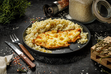 Grilled hawaiian chicken with cheese, ananas and boiled rice served on a black plate
