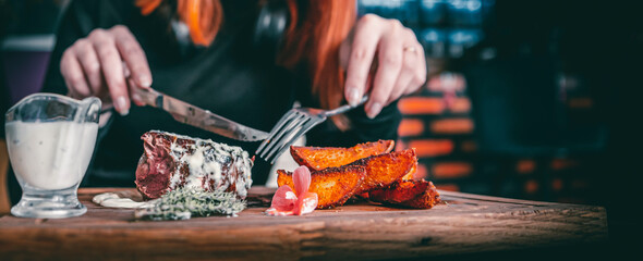 woman hands with fork and knife eating beef steak in cafe