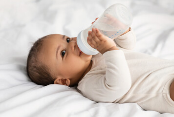 Cute little African American baby drinking water from bottle
