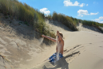Boy sits in the dunes and plays with the sand