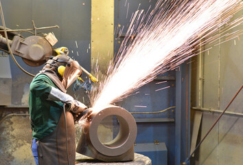 Workers in protective equipment in a foundry work on a casting with a grinding machine at the...