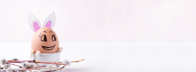 Easter egg reminding cute bunny and willow twig on the white table. Festive background. Web banner with copy space