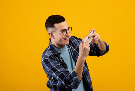 Online Gaming Concept. Portrait Of Positive Young Guy Playing Video Games On Smartphone Over Orange Studio Background