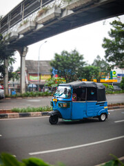 A bajaj car crosses the middle of Jakarta Indonesia's road, above which there is a bridge for people to cross safely